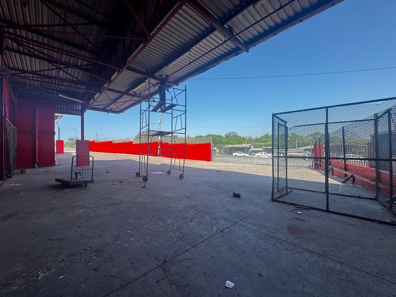 Large industrial covered loading or storage area featuring concrete flooring, steel structural supports, and perimeter security fencing.