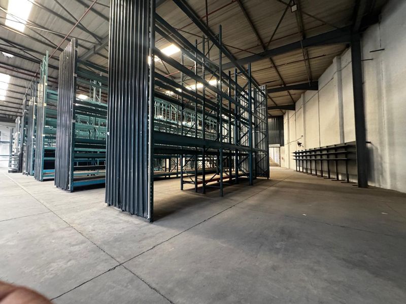 Spacious industrial warehouse featuring high ceilings with exposed steel trusses, heavy-duty steel racking systems, and durable concrete flooring.