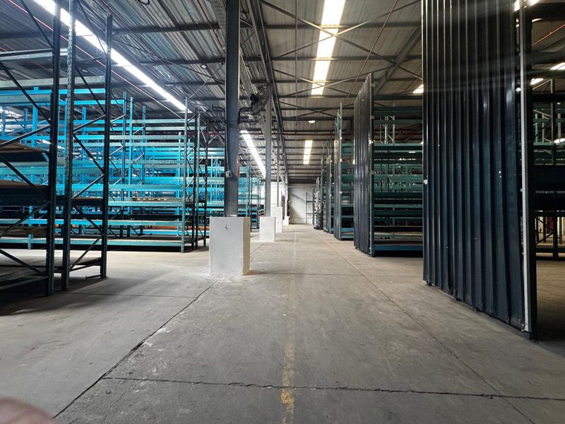 Spacious industrial warehouse interior featuring extensive steel racking systems, concrete flooring, and high ceilings with integrated skylights for natural illumination.