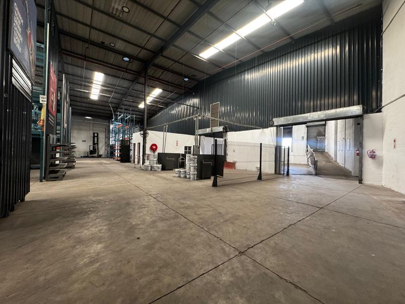 Spacious industrial warehouse featuring high ceilings, concrete flooring, integrated loading ramp, and roller shutter access, suitable for storage or manufacturing operations.