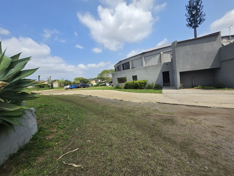 Exterior view of a commercial property featuring a concrete driveway, landscaped grounds, and a prominent cell tower structure.