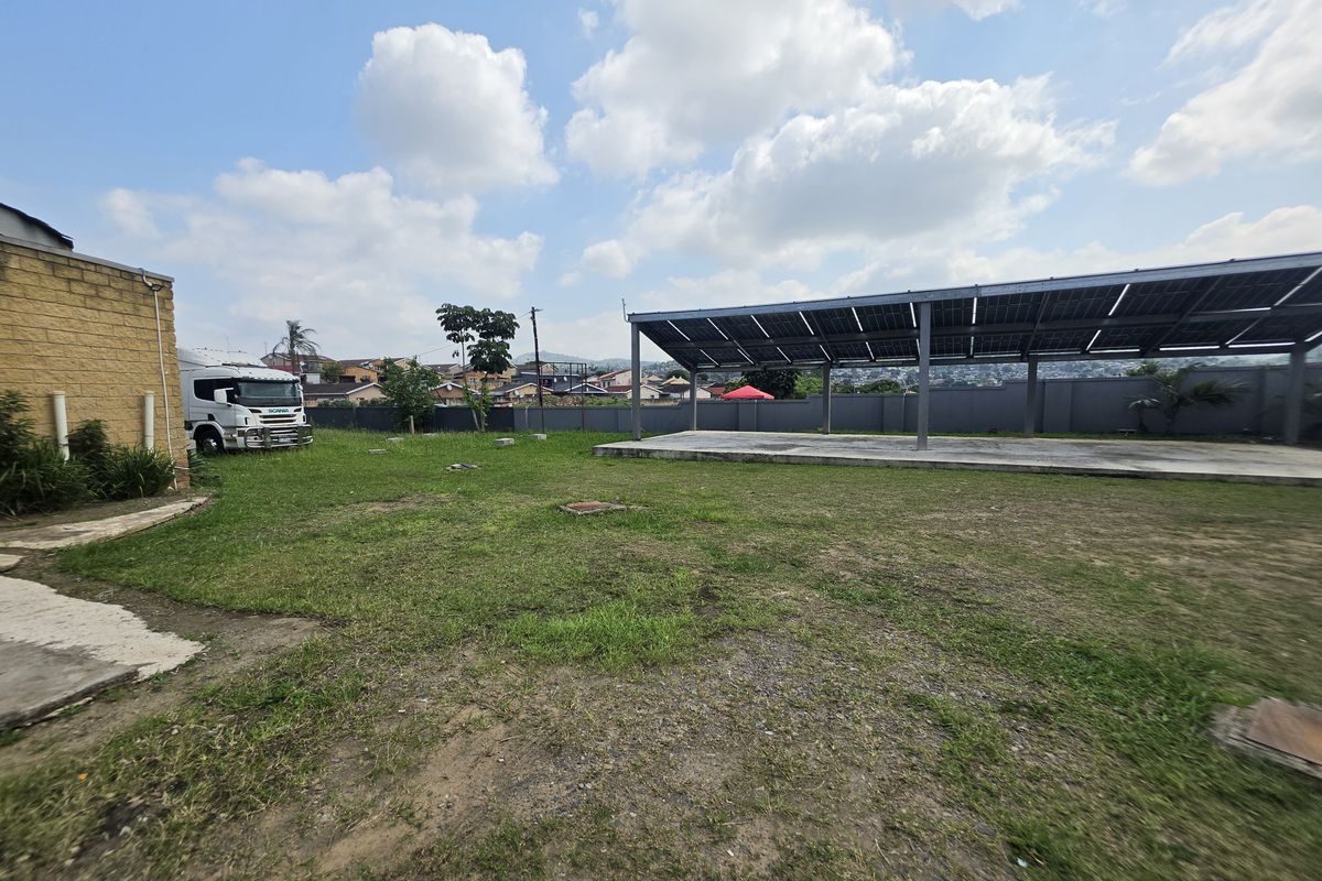 Spacious rear yard featuring a large concrete slab covered by a solar panel structure, enclosed by a perimeter wall.