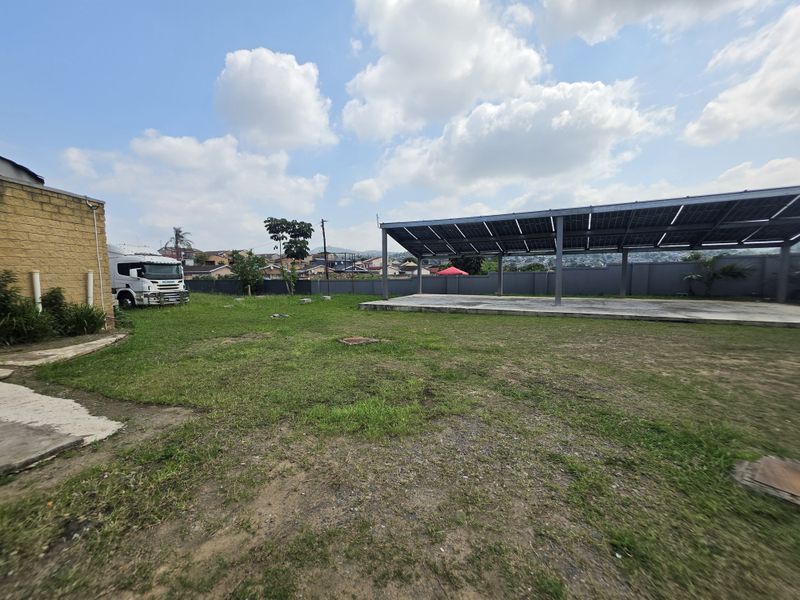 Spacious rear yard featuring a large concrete slab covered by a solar panel structure, enclosed by a perimeter wall.