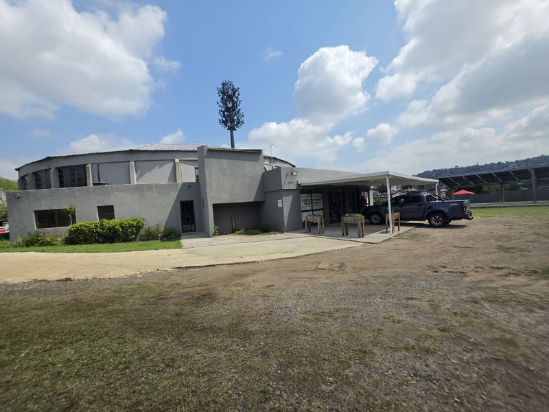 Front exterior view of a commercial building featuring a covered entrance, concrete driveway, and an integrated telecommunications tower on the roof.