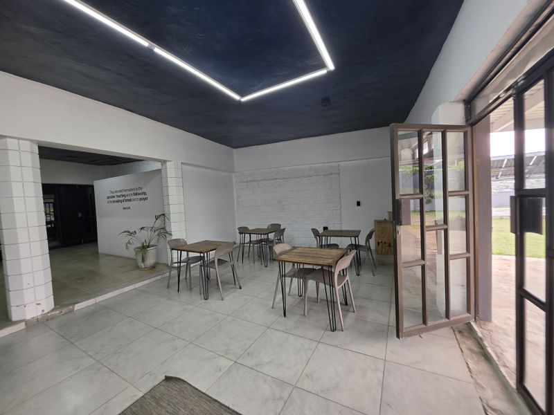 Open-plan commercial space featuring tiled flooring, modern linear lighting, and exposed brick accents with direct access to an outdoor area.