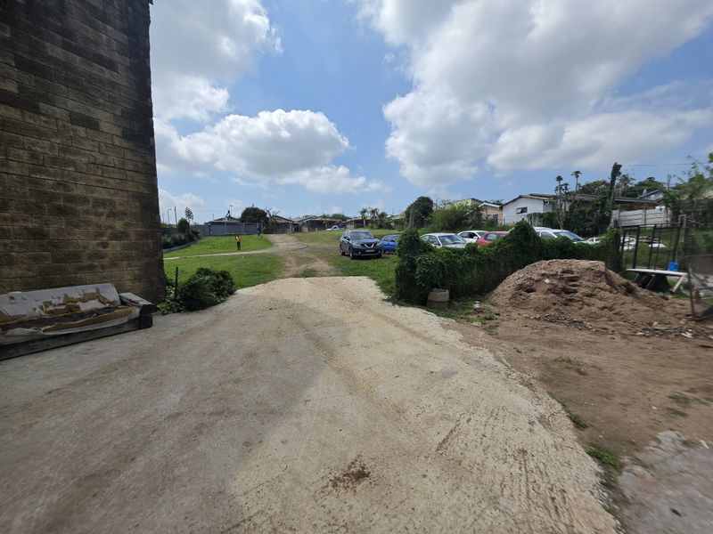 An outdoor rear area featuring a concrete driveway leading to a grass lawn and surrounding residential properties.