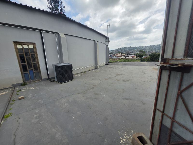 Rear exterior area featuring concrete paving, an external air conditioning unit, and access via a timber door and metal security gate.