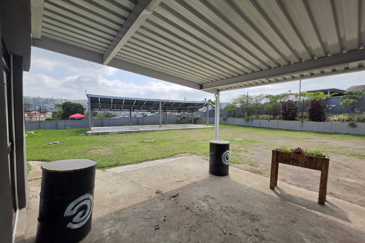 A covered outdoor patio area featuring a concrete floor and a metal roof, overlooking a spacious garden with a solar panel installation.