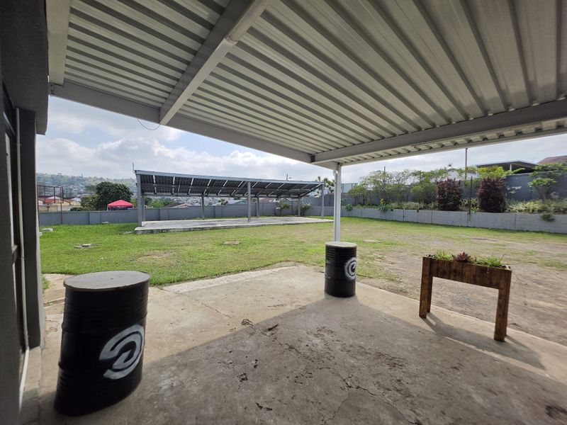 A covered outdoor patio area featuring a concrete floor and a metal roof, overlooking a spacious garden with a solar panel installation.