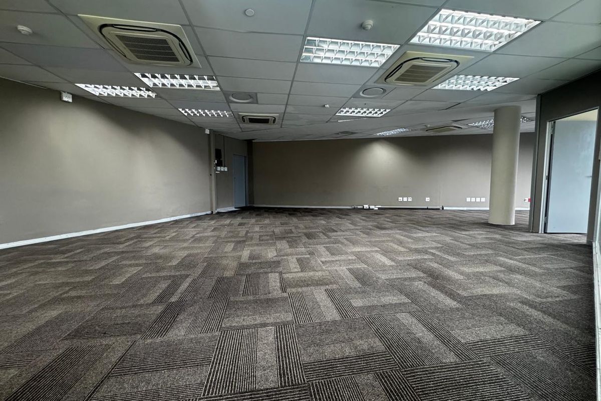 Spacious open-plan office area featuring neutral wall finishes, carpet tile flooring, recessed lighting, and integrated ducted air conditioning units.
