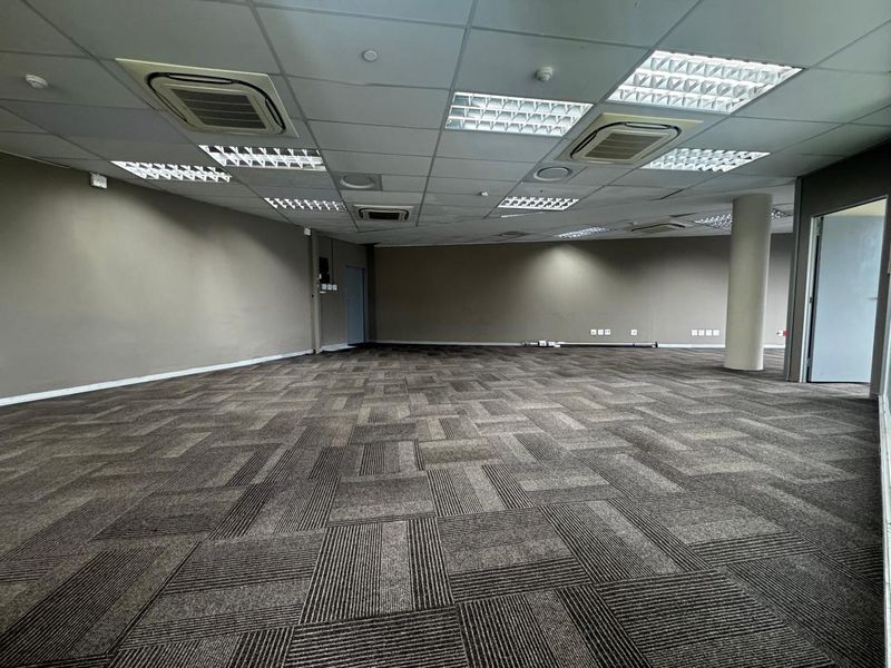 Spacious open-plan office area featuring neutral wall finishes, carpet tile flooring, recessed lighting, and integrated ducted air conditioning units.