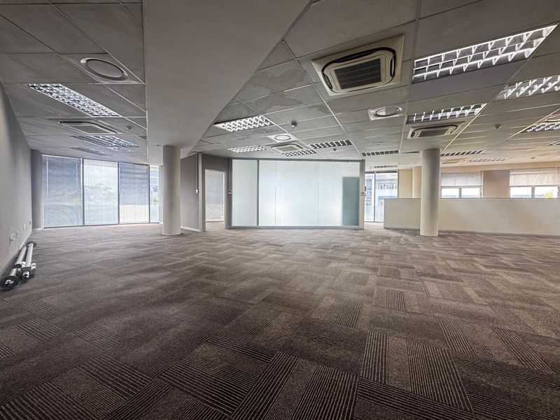 Spacious open-plan office area featuring carpeted flooring, suspended ceilings with integrated lighting, central air conditioning, and a glass-partitioned meeting room.