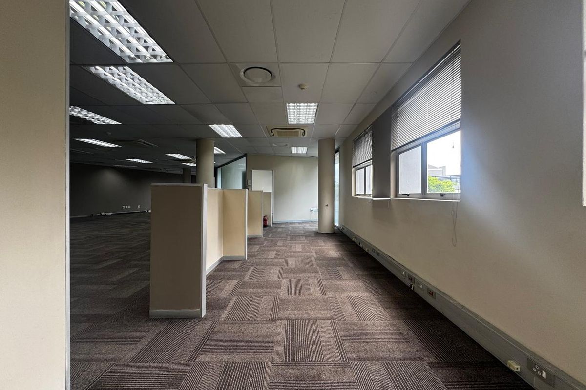Spacious open-plan office area featuring suspended ceilings, recessed lighting, carpet tiles, and built-in cubicle partitions, offering a functional workspace layout.