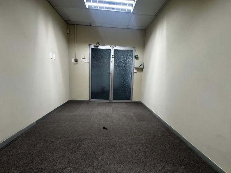 An empty office space featuring a drop ceiling with fluorescent lighting, carpeted flooring, and a double glass entrance door.