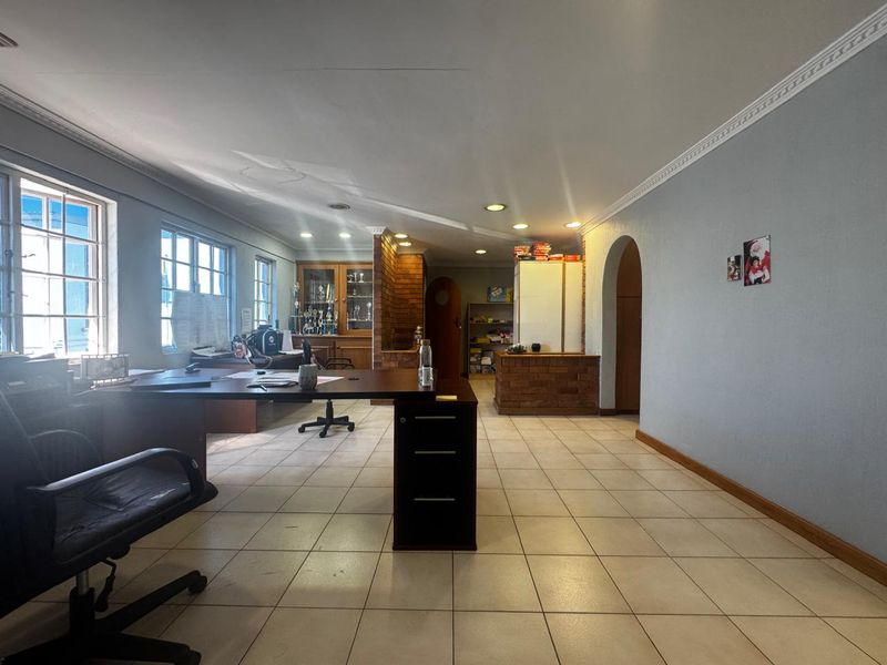 Spacious office area featuring tiled flooring, recessed lighting, crown molding, and a distinctive brick partition wall, offering a functional workspace layout.