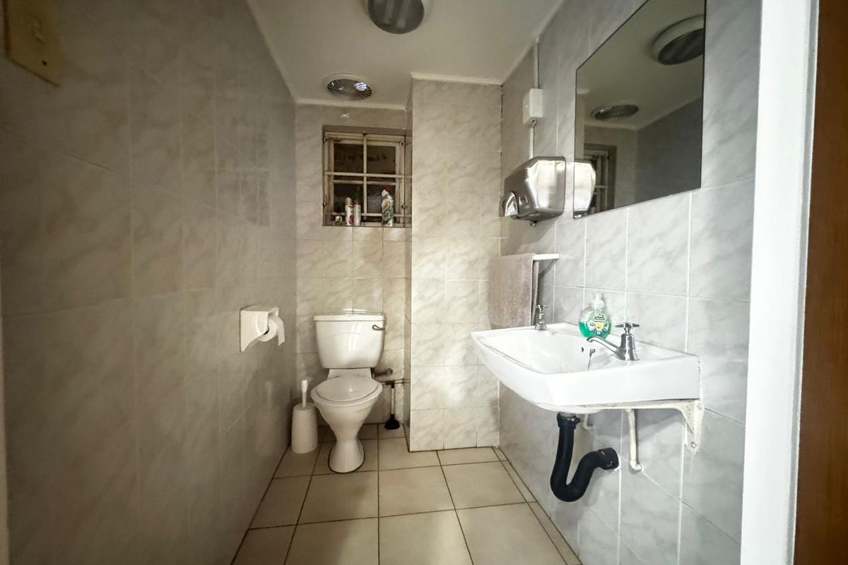 A functional industrial-style bathroom featuring tiled walls and flooring, a wall-mounted basin, and a standard toilet.