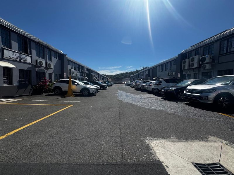 Exterior view of an industrial complex featuring a paved parking area between two rows of commercial units with external air conditioning units.