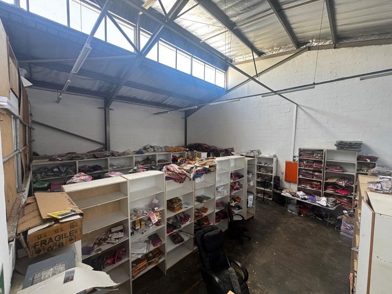 Industrial warehouse or storage space featuring high ceilings with exposed steel trusses, clerestory windows for natural light, and durable concrete flooring.