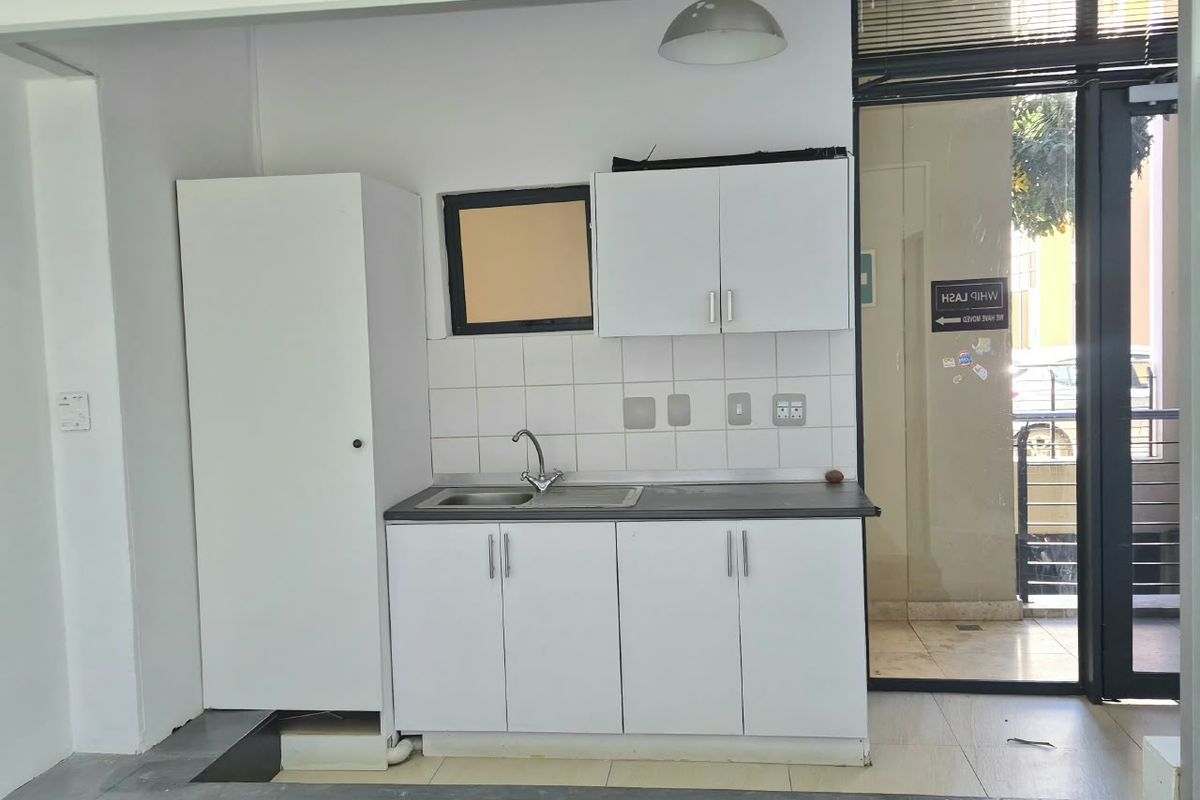 A compact kitchenette featuring white built-in cabinetry, a stainless steel sink, and a tiled backsplash, conveniently located near a glass entrance door.
