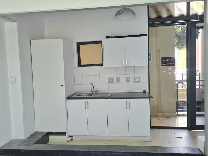 A compact kitchenette featuring white built-in cabinetry, a stainless steel sink, and a tiled backsplash, conveniently located near a glass entrance door.