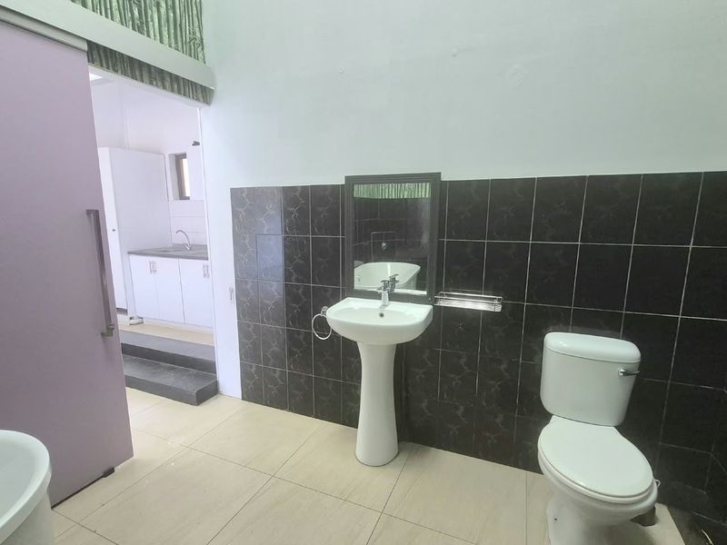A functional bathroom featuring a pedestal basin, toilet, and dark tiled wall accents, with a sliding door leading to an adjacent utility area.