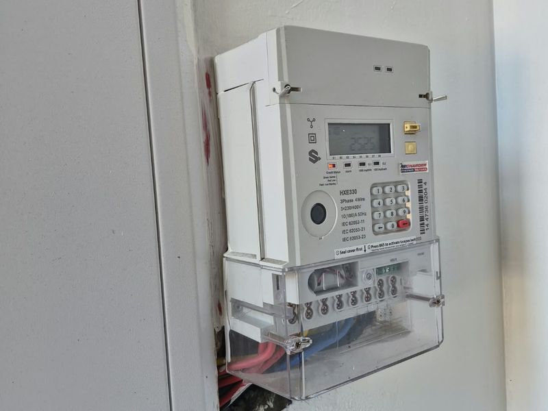 A wall-mounted prepaid electricity meter showing visible damage to the surrounding wall plaster and exposed wiring.