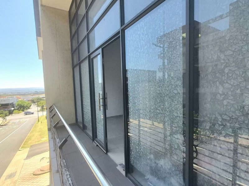 A modern office balcony featuring a metal balustrade, large glass facade with privacy film, and tiled flooring overlooking the street.