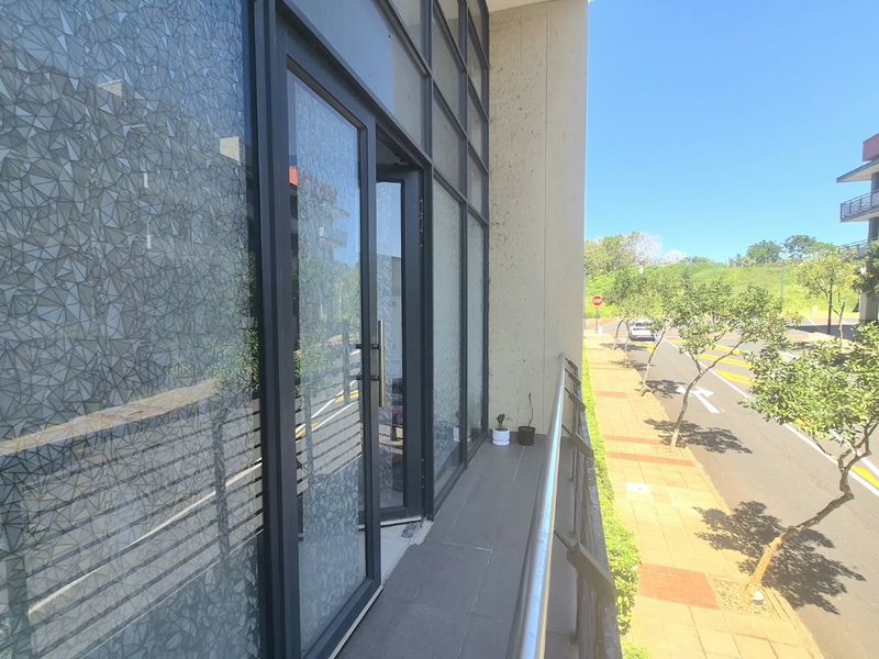 A modern office balcony featuring a glass facade, metal railing, and tiled flooring, overlooking the street.