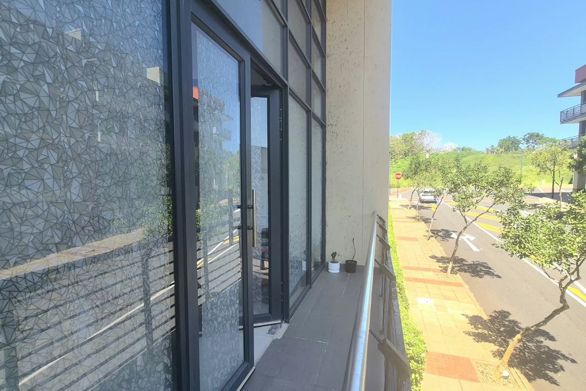 A modern office balcony featuring a glass facade, metal railing, and tiled flooring, overlooking the street.
