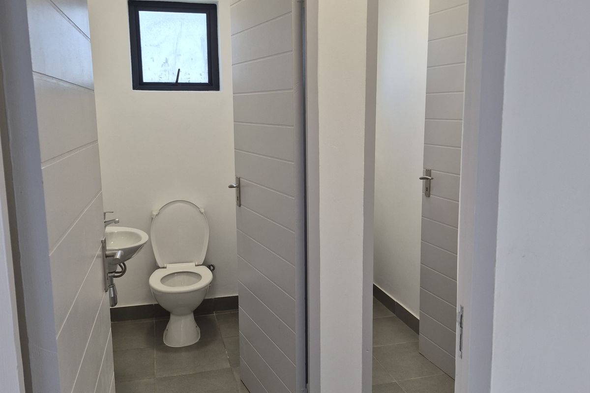 A clean, modern industrial restroom facility featuring tiled flooring, white walls, and individual cubicles with contemporary fixtures.