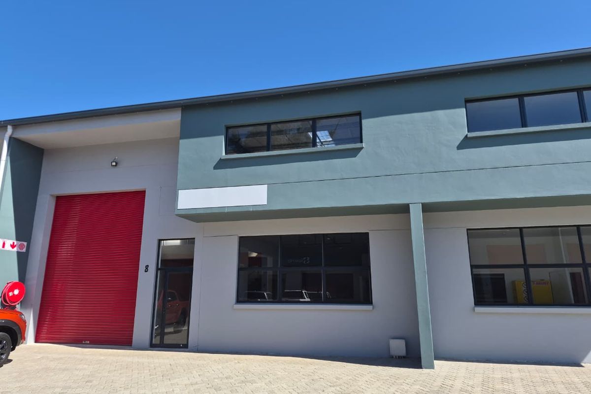 Modern industrial unit featuring a large red roller shutter door, glass-paneled windows, and paved exterior frontage.