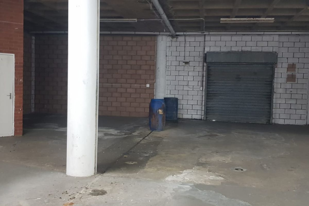 An expansive, open-plan commercial warehouse space featuring exposed brick and block walls, concrete flooring, a structural column, and a secure roller shutter door.