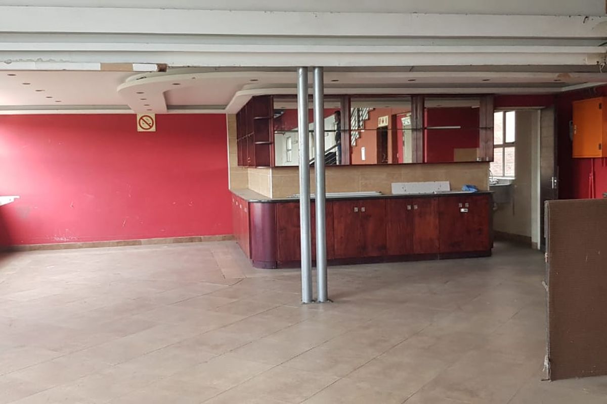 A vacant commercial space featuring a built-in bar counter, tiled flooring, and red accent walls, suitable for a hospitality or office layout.