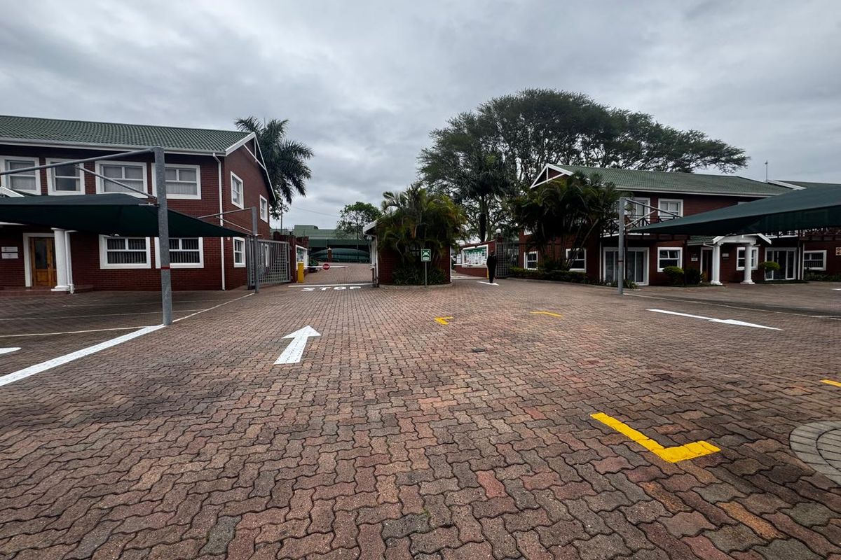 Exterior view of an office complex featuring a paved parking area with shade cloth carports and brick building facades.