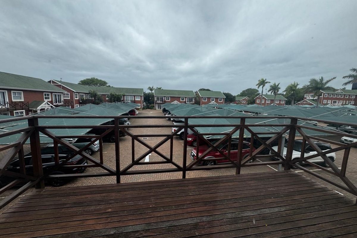 Elevated wooden balcony overlooking a complex parking area with covered carports and surrounding residential buildings.