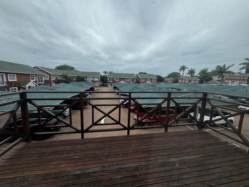 Elevated wooden balcony overlooking a complex parking area with covered carports and surrounding residential buildings.