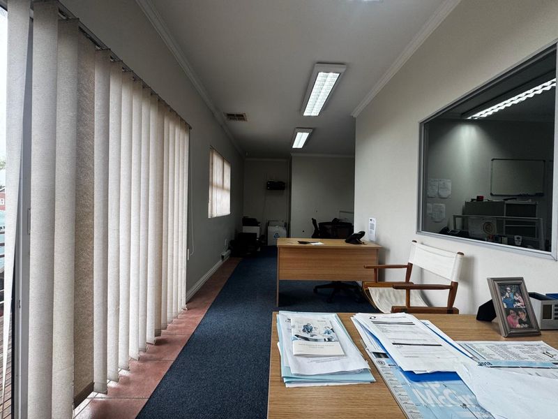 A functional office space featuring carpeted flooring, vertical blinds, and an internal glass partition, providing a professional environment with ample natural light.