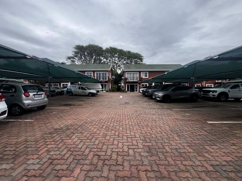 Exterior view of the office complex featuring a paved parking area with shade cloth carports and two-story brick buildings with balconies.