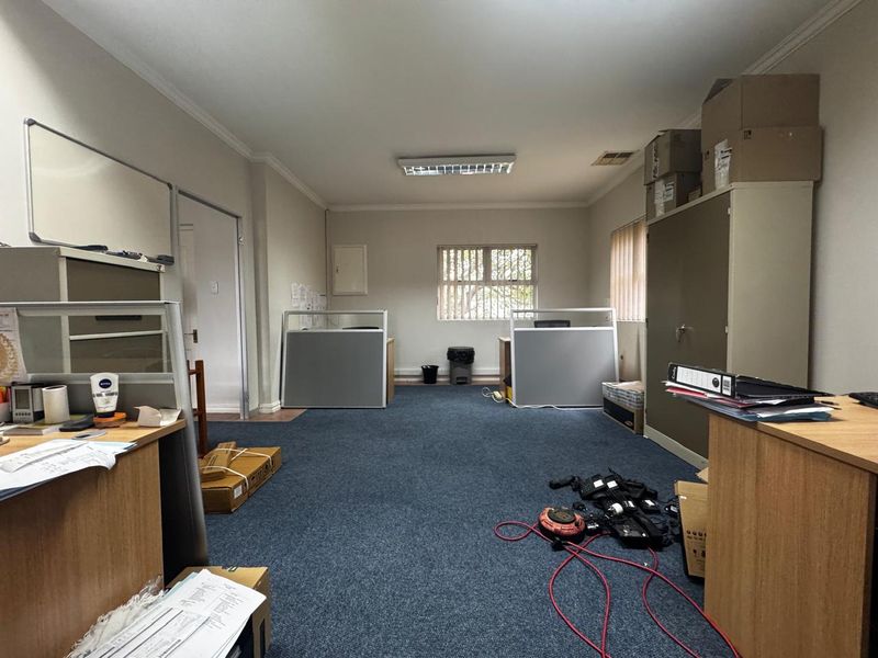 A functional office space featuring carpeted flooring, fluorescent lighting, and security bars on the window, providing a practical work environment.