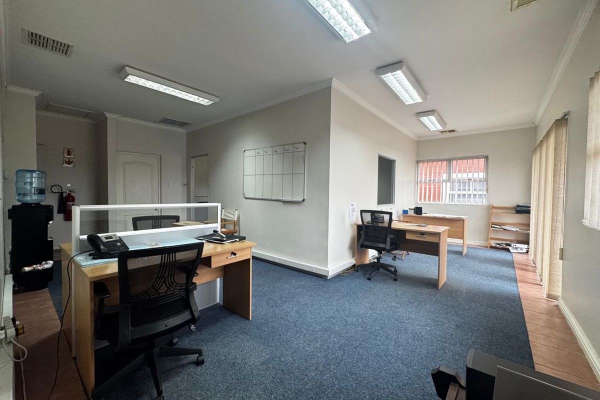 A functional office space featuring carpeted flooring, fluorescent lighting, and wall-mounted whiteboard, providing a practical environment for professional work.