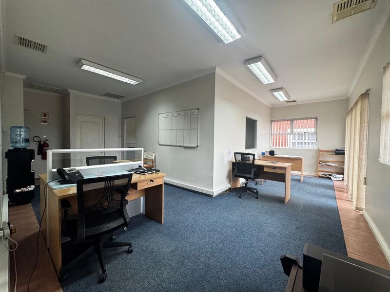 A functional office space featuring carpeted flooring, fluorescent lighting, and wall-mounted whiteboard, providing a practical environment for professional work.