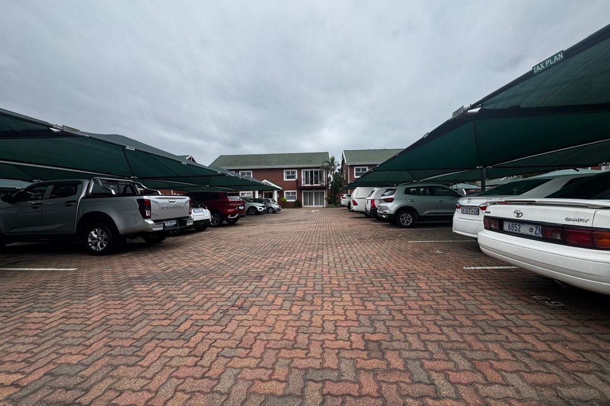 A paved parking area featuring multiple shade cloth carports serving the office building complex.