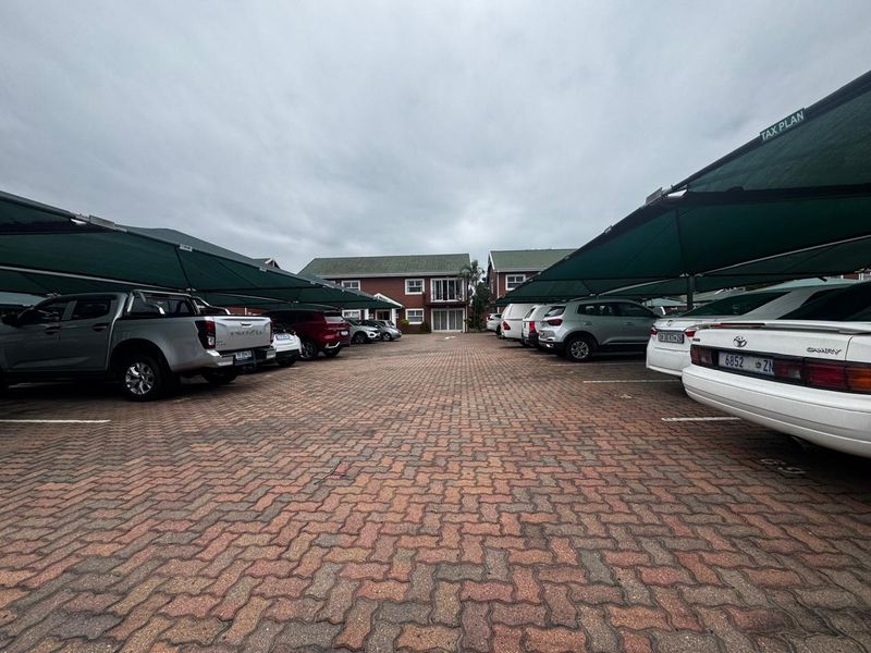 A paved parking area featuring multiple shade cloth carports serving the office building complex.