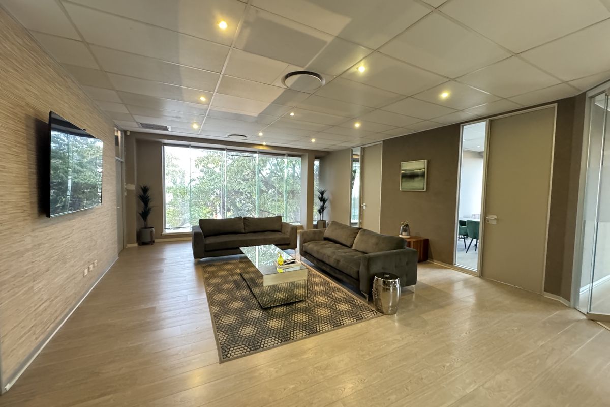 A modern office lounge area featuring a wood-panelled feature wall, suspended ceiling with recessed lighting, and large windows providing natural light.