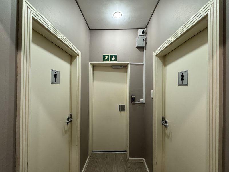 A clean office hallway featuring separate male and female restroom access and a clearly marked emergency exit door.