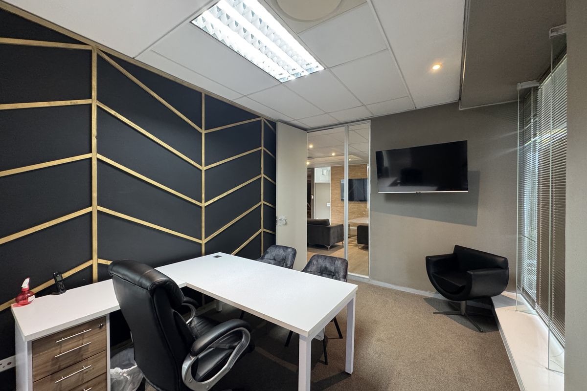 A modern office space featuring a decorative accent wall, glass partition, carpeted flooring, and integrated lighting, providing a professional and functional work environment.