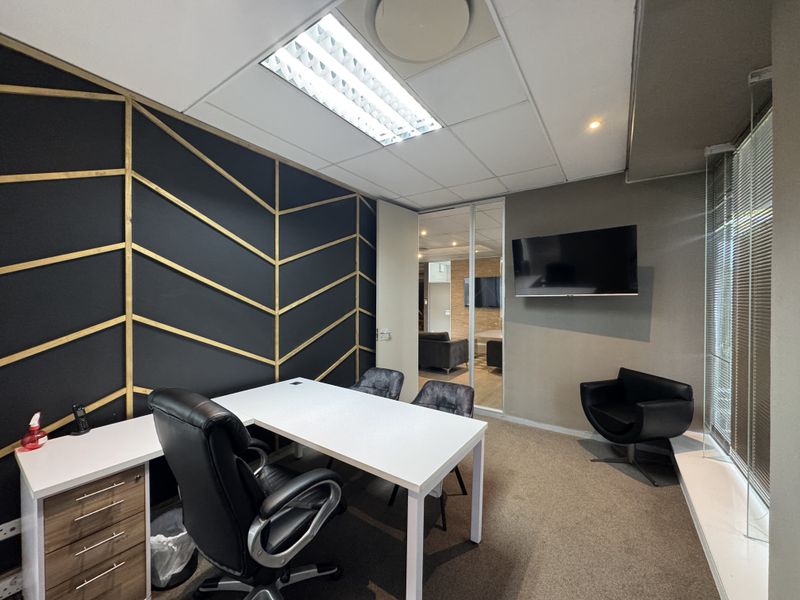 A modern office space featuring a decorative accent wall, glass partition, carpeted flooring, and integrated lighting, providing a professional and functional work environment.