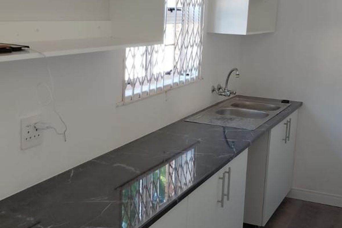 A clean, functional kitchenette featuring white cabinetry, dark marble-effect countertops, a stainless steel sink, and modern laminate flooring.