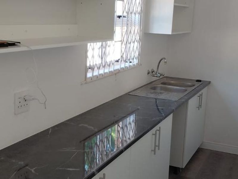 A clean, functional kitchenette featuring white cabinetry, dark marble-effect countertops, a stainless steel sink, and modern laminate flooring.