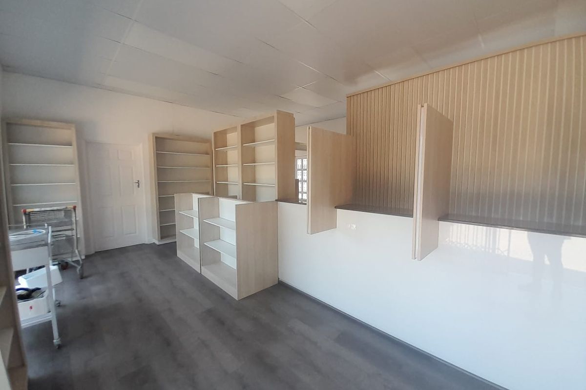 A bright, open-plan retail space featuring modern laminate flooring, built-in shelving units, and a professional service counter with panelled wall detailing.